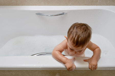 Toddler baby climbs over the edge of the tub at the risk of falling. The danger of leaving a child...