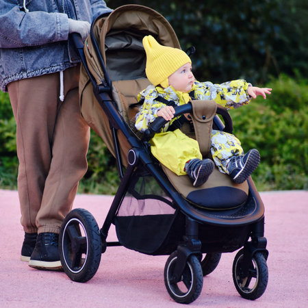 Happy toddler baby boy in stroller with mother on a walk in the park. A child in warm clothes...