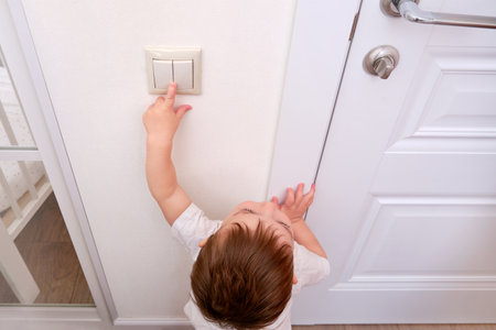 Toddler baby reaches for the light switch, child hand turns on the lamp close-up. White light switch in home room and baby handの写真素材