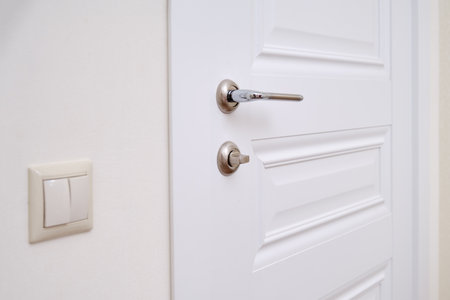 A white door with a lock in the home room and a light switch. Metal door handle and plastic light switch in the apartmentの写真素材