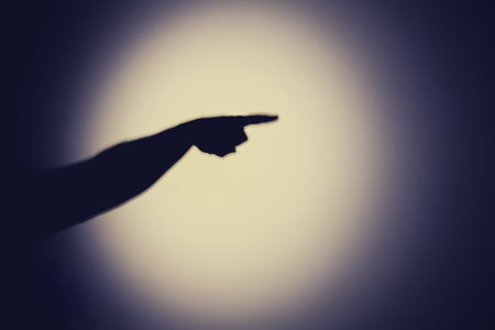Shadow of a hand from the night light of a flashlight on a white wall. Dark silhouette of a man hands from the light of a lampの写真素材