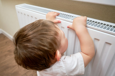 Toddler baby holding on to the radiator, child hand on the heating system close-up. White radiator for heating the home room and children's handの写真素材