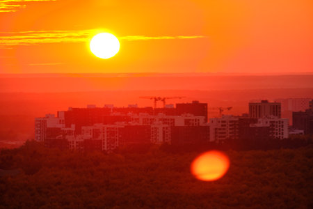 A big red sun in the sunset sky over the roofs of buildings, urban landscape. Evening sky in bright sunlight over the twilight cityの写真素材