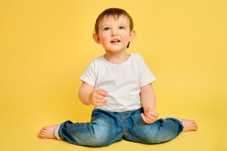 Portrait of a happy toddler baby in full length on a studio yellow background. Smiling child sitting...