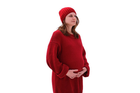 A happy pregnant woman in a knitted sweater and a hat walks in the park, a winter forest with trees in the snow, isolated on a white backgroundの写真素材