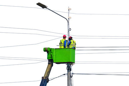 Electrical engineers repair the line standing on the crane platform at a high pole, isolated on a white backgroundの写真素材