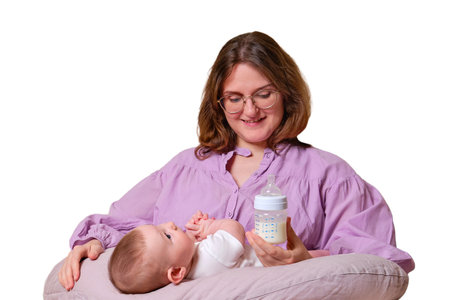 Woman mother feeds infant baby formula from a bottle, isolated on a white background. Kid aged six monthsの写真素材