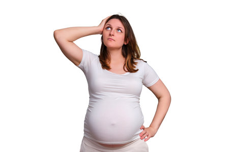 Thoughtfulness and doubts of a pregnant woman, studio shot on a white backgroundの写真素材