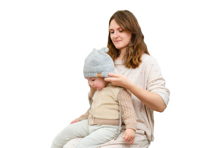 Mother puts a warm scarf on the toddler baby, isolated on a white background. Woman mom dressing warm clothes on child for winter walk in cold weather. Kid aged one year and three monthsの写真素材