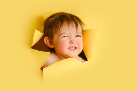 Shame baby in a hole on a paper yellow background. Torn child's head studio background, copy space....