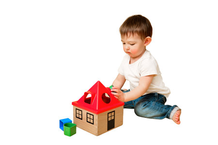 Toddler baby is playing sorter logic educational games with geometric shapes on a studio isolated on a white background. Happy child play with educational toy house. Kid aged one year four monthsの写真素材