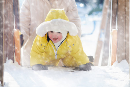 Toddler baby boy is playing in the snow on the winter playground. Happy child in a yellow snowsuit in kindergarten. Kid age one year eight monthsの写真素材