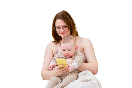 A mother woman shows a mobile phone to an infant baby boy, isolated on a white background. Mom and son look at the smartphone screen. Kid aged six monthsの写真素材