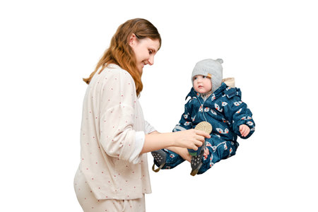 Mother puts a warm scarf on the toddler baby, isolated on a white background. Woman mom dressing warm clothes on child for winter walk in cold weather. Kid aged one year and three monthsの写真素材