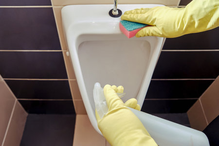 Cleaning in a public toilet cafe, a man hand in yellow gloves wipes the urinal with a spongeの写真素材