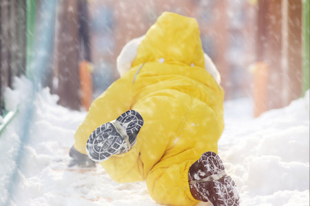 Toddler baby boy is playing in the snow on the winter playground. Happy child in a yellow snowsuit in kindergarten. Kid age one year eight monthsの写真素材