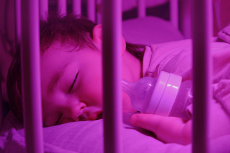 Toddler baby sleeps lying with a bottle of milk in a crib. Funny child boy sleeps at night in the nursery. Kid age one year eight monthsの写真素材