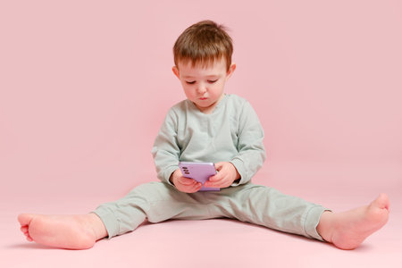 Happy toddler baby with mobile phone on studio pink background. Child boy holding a smartphone in his hands. Kid age one year eight months, full heightの写真素材