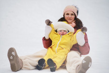 A mother woman with a toddler baby rides an ice sled in a snowy park. Mom and son boy ride in winter from a snow slide. Kid aged one year eight monthsの写真素材