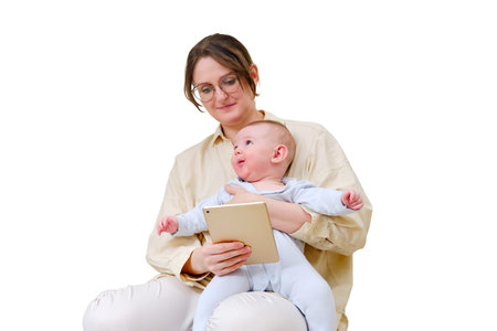 Happy woman mother with infant baby watching in digital tablet while sitting on home sofa in living room, isolated on a white background. Kid aged six monthsの写真素材