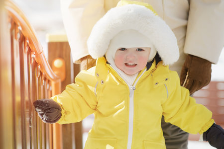 Portrait of a toddler baby in warm yellow clothes on a winter playground. Happy baby boy in snowsuit standing in the snow in kindergarten. Kid age one year eight monthsの写真素材