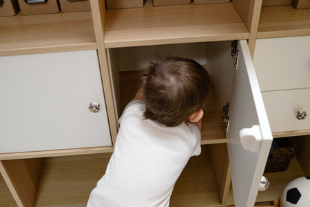 Toddler baby opens the closet door in the home living room. A small child opens a shelf drawer. Kid aged one year eight monthsの写真素材