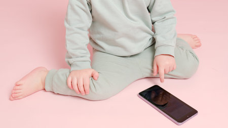 Happy toddler baby with mobile phone on studio pink background. Child boy holding a smartphone in his hands. Kid age one year eight monthsの写真素材
