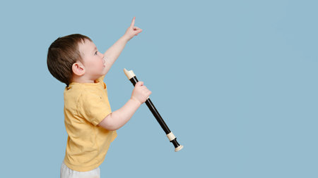 Happy toddler baby with a musical instrument flute on a studio blue background. Child boy learning music with wind instrument. Kid age one year eight monthsの写真素材