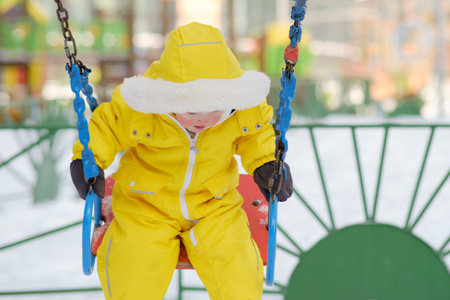 Toddler baby falls from a swing on the playground. A dangerous situation for a child in kindergarten. Kid age one year eight monthsの写真素材