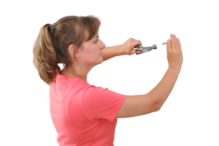 A young woman with a hammer in her hands, isolated on a white background. Repair yourself in the new house, isolated on a white background. Woman hammering nails into the wall.の写真素材