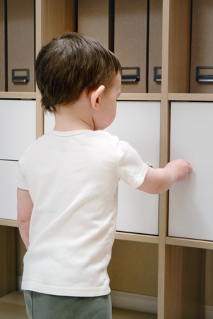 Toddler baby opens the closet door in the home living room. A small child opens a shelf drawer. Kid aged one year eight monthsの写真素材
