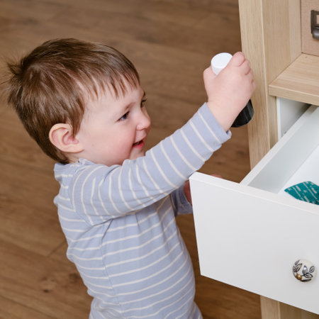 Toddler baby opened a cabinet drawer with pills and a vial of potion. Child boy holding medicine bottle standing in home living room. Kid age one year nine monthsの写真素材