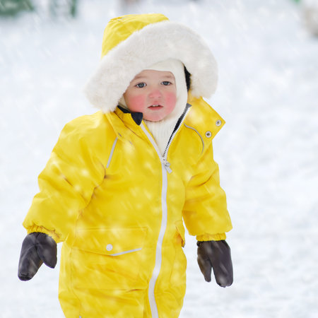 Portrait of a toddler baby in warm yellow clothes on a winter playground. Happy baby boy in snowsuit standing in the snow in kindergarten. Kid age one year eight monthsの写真素材