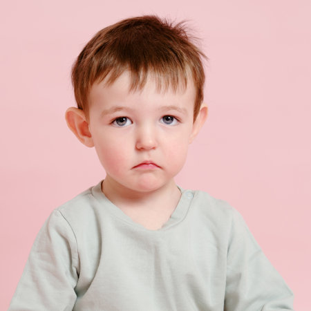 Sad toddler baby on studio pink background, copy space. Unhappy child boy face close-up. Kid age one year eight monthsの写真素材