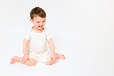 A happy baby is sitting on a studio white background. Full-length portrait of a smiling child. Kid aged about two years (one year nine months)の写真素材