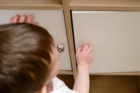 Toddler baby opens the closet door in the home living room. A small child opens a shelf drawer. Kid aged one year eight monthsの写真素材