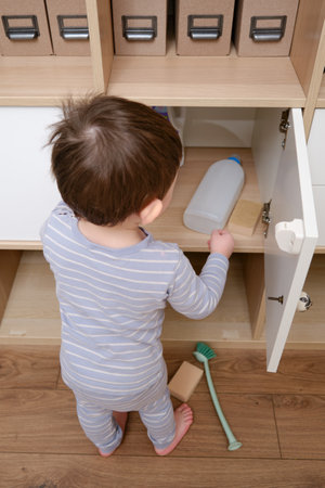 Toddler baby plays with household chemicals and detergent from the closet. Child boy with detergent bottle in home living room. Kid age one year nine monthsの写真素材