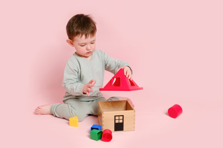 Happy toddler baby plays sorter with geometric shapes on studio pink background. Child boy plays educational toys. Kid age one year eight months, full heightの写真素材