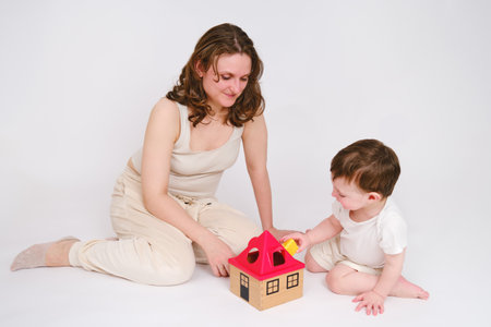 Happy baby with mother play educational toys on studio white background. Portrait of a smiling child with mom and playing while sitting on the floor. Kid about two years old (one year nine months)の写真素材