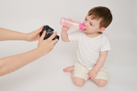 Woman mother photographs baby on photo camera, studio white background. Mom blogger shoots a video from a child for a blog. Kid about two years old (one year nine months)の写真素材