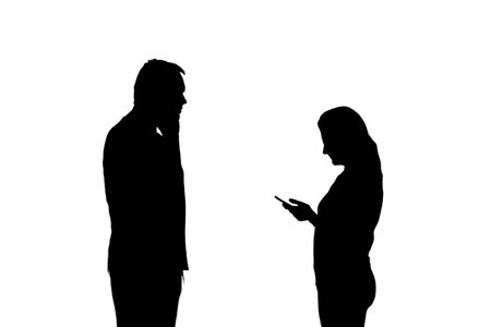 Silhouette of a man and a woman with phones, isolated on a white background. Couple husband and wife having relationship problems in the evening lightの写真素材