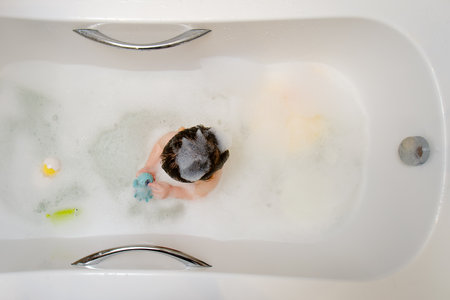 A happy child is playing with toys while sitting in a white homemade bathtub. Little toddler baby boy bathes in a bubble bath. Kid aged one year six monthsの写真素材