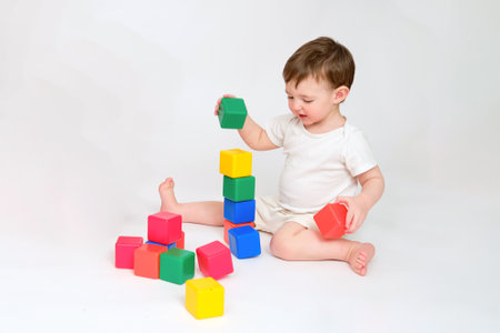 Happy baby play educational toys on studio white background. Portrait of a smiling child playing while sitting on the floor. Kid about two years old (one year nine months)の写真素材