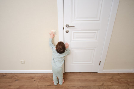 Little baby turns on the light by pressing the switch. Small child turns off the electric light at the white door. Kid aged two yearsの写真素材