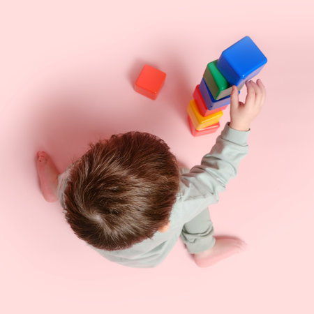 Happy toddler baby plays with cubes on studio pink background. Child boy builds a tower of toys. Kid age one year eight monthsの写真素材