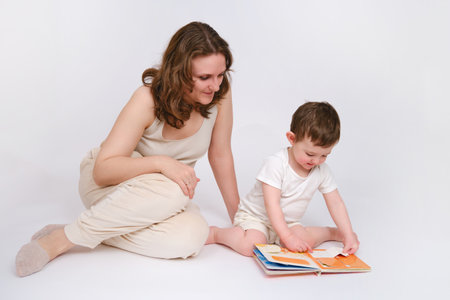Happy baby with mother reading a book on studio white background. Portrait of a smiling child with mom. Kid about two years old (one year nine months)の写真素材