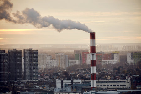 Smoke from a tall chimney over a winter city with houses in the snowの写真素材