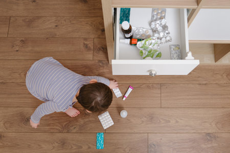 Toddler baby opened the cabinet drawer with pills and medicine. Child boy holding a pack of pills in the home living room. Kid age one year nine monthsの写真素材
