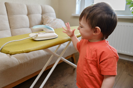 Child left without supervision may get burned or hurt as the baby plays dangerously with a hot iron in the living room of the home. Kid aged about two years (one year ten months)の写真素材