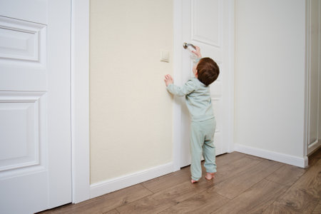 Little baby opens the door. Child pulls the door handle with the lock closed. Kid aged two yearsの写真素材